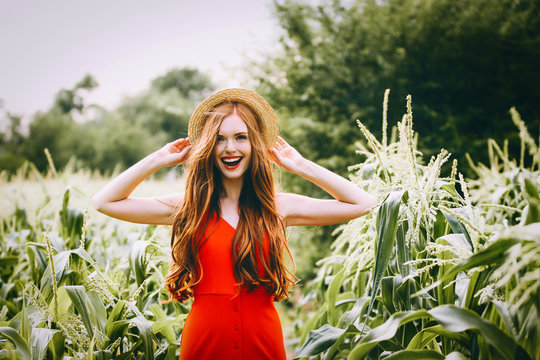 red-haired girl with freckles in red dress walking on a field of corn she is smiling a
 sweet smile on her head Summer panama