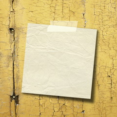 Close-up of one blank square old paper sheet frame with adhesive tape on yellow scratched wooden boards background