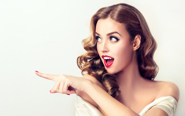 Fototapeta premium Woman surprise showing product .Beautiful girl with curly hair pointing to the side . Presenting your product. Expressive facial expressions