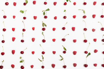 many raspberries and cherries arranged on white