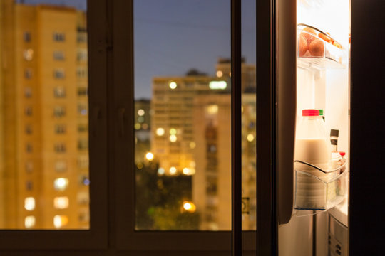 Open door of home fridge and urban view in night
