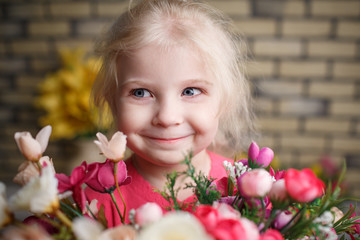 Portrait of a beautiful little girl with flowers on background of brick wall