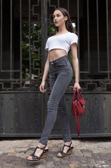 Beautiful brunette young woman wearing jeans and walking on the street . Red bag in woman hand....