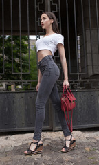 Beautiful brunette young woman wearing jeans and walking on the street . Red bag in woman hand....