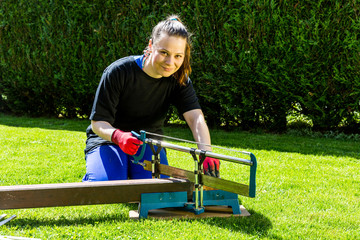 Girl is sawing a wooden beam in the garden