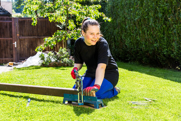 Girl is sawing a wooden beam in the garden