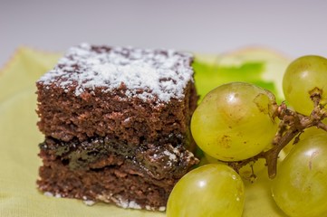 Chocolate sponge cake with icing sugar and grapes on the yellow tablecloth