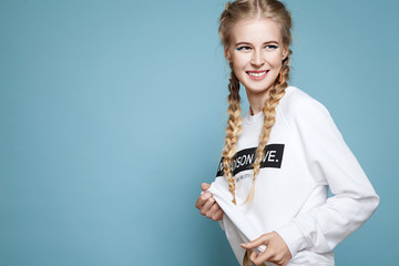 Young cheerful girl in a white sweatshirt with braids on a blue background