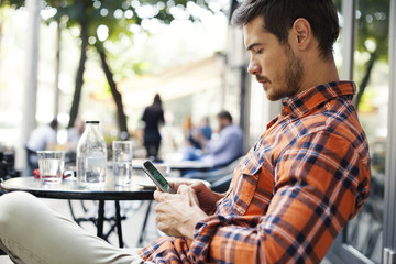 Attractive Man Sitting In Cafe Bar And Holding Mobile Smart Phone