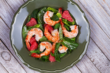 Shrimp, grapefruit and spinach salad in green plate. View from above, top studio shot