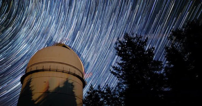Rozhen astronomical observatory under the night sky stars. Blue sky with hundreds of stars of the Milky way. Observatory in a pine trees forest in the mountain. 4k timelapse in comet mode. Tilting