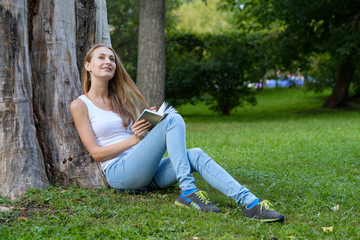 Obraz premium Young woman reading a book in the park and dreaming