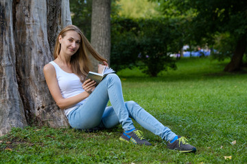Young woman reading a book in the park and dreaming