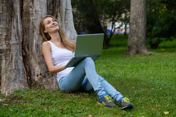 Young woman using laptop in the park sitting on the grass