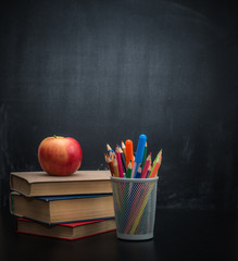 Background blackboard chalk, books, colored pencils and an apple