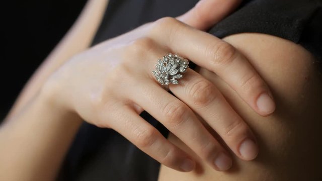 hand of woman lying on her shoulder, big sparkling silver ring is on finger, close-up