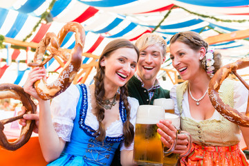 Drei Freunde auf der Dult oder Oktoberfest beißen in Riesenbrezen und trinken Bier im Bierzelt