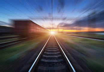 Railway station with cargo wagons and train light in motion at sunset. Railroad with motion blur effect. Railway platform. Heavy industry. Conceptual background