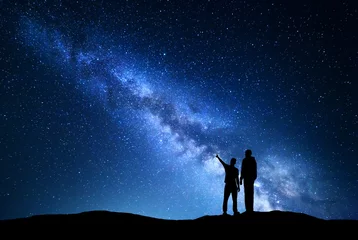 Foto op Aluminium Milky Way with silhouette of men. Father and a son who pointing finger in night starry sky on the mountain. Night landscape. Silhouette of family on the background of beautiful galaxy. Space.  © den-belitsky