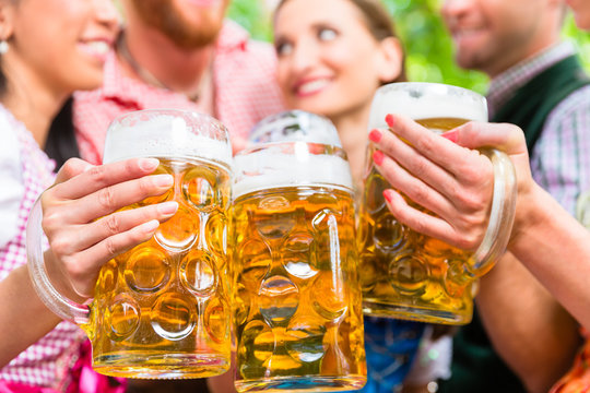 Freunde, zwei M&auml;nner, drei Frauen, stehen im Biergarten mit Ma&szlig;kr&uuml;gen