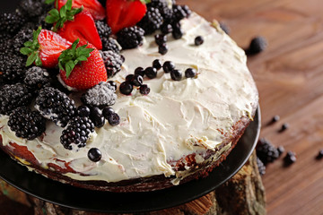 Appetizing cake decorated with berries on wooden background