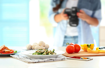 Plate with salad on table and girl photographing at kitchen. Food blogger concept
