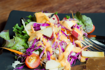 Salad in black plate, on the wood table.
