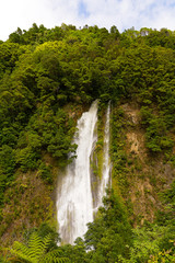 Naklejka premium Scenic waterfall near Furnas in Azores, Portugal. Rain forest on a hill and waterfall in sight near a road from Furnas to Ribeira Quente on Sao Miguel Island.