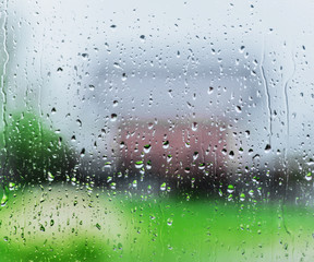 Rain drops on glass of a window, an outline of the one-storey house