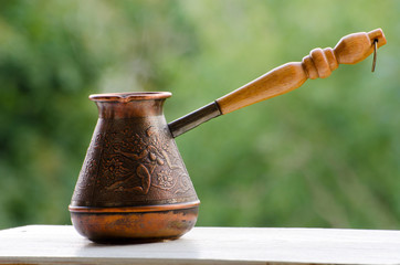 Copper Cezve with hot coffee on a windowsill, blurred green background