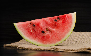 Large slice of ripe watermelon on sackcloth, black background