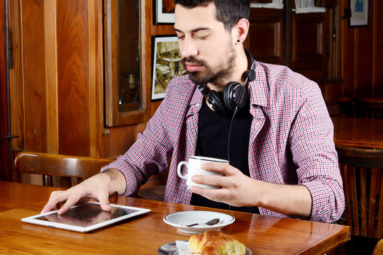 Man drinking coffee with headphones and digital tablet.
