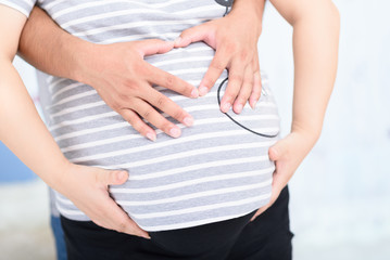 A couple making a heart shape on the pregnant belly with theri h