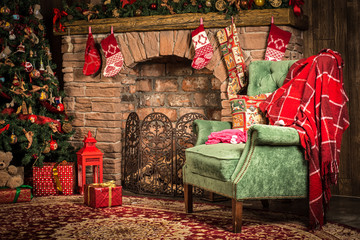Рождественские декорации: зеленое кресло у камина, елка с игрушками и подарки 