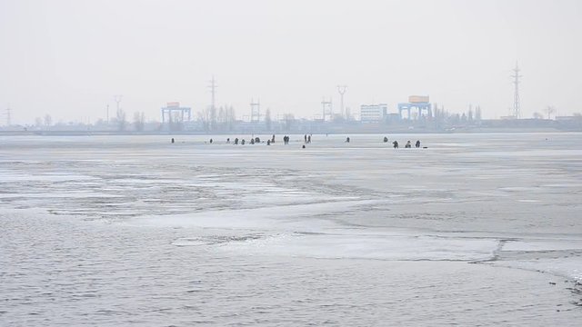 Winter fishermen angle on ice of partially frozen water storage basin on background of hydroelectric power plant or station in Vyshgorod near Kiev, Ukraine on Dnieper river