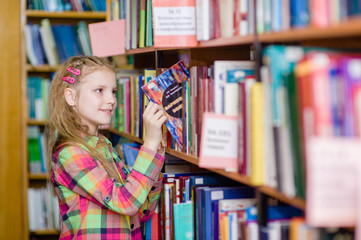 young girl chooses a book in the library