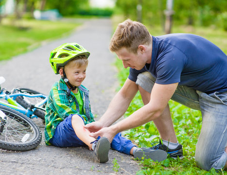 father putting band-aid on young boy's injury who fell off his bike