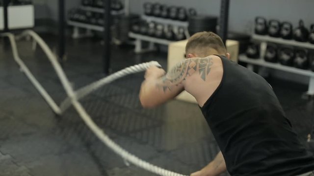 Young adult man doing crossfit workout with ropes led