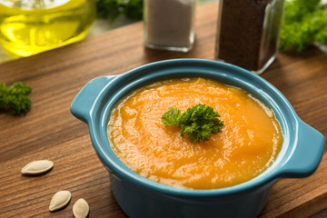 Pumpkin soup in bowl with fresh pumpkins, garlic and parsley