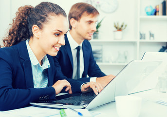 Glad business female assistant wearing formalwear using laptop