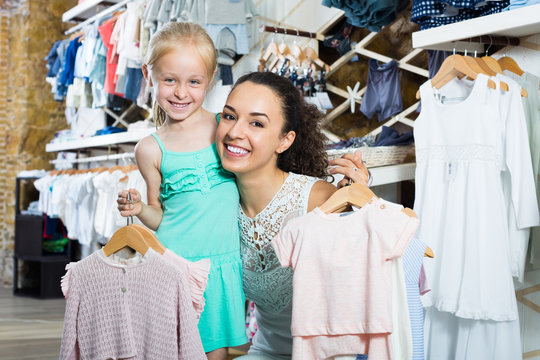 Smiling young woman with small girl holding clothes
