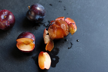 Four ripe peeled and sliced juicy plums lying on a black table. Summer in the village, the time of harvest. Plums are dark purple, sweet and full of juice. Juice splashed around. Rural weekend.