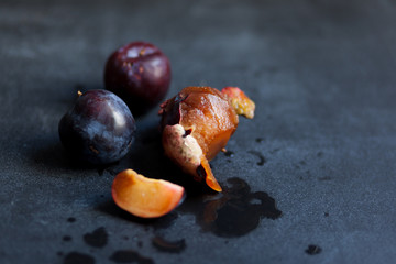 One plum slice, one peeled plum and a few whole ripe plums lying on a black table. Autumn in the village, the time of harvest. Plums are dark purple, sweet, juicy and organic. Juice splashed around.