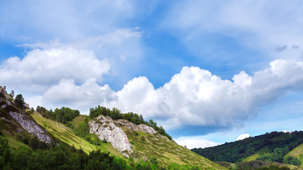 Mountain range with trees and vegetation under blue sky and clouds. (Russia)