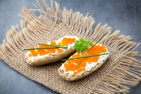 Bread with fresh cream cheese and red caviar on table.