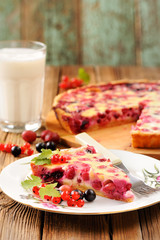 Gooseberry pie slice on white plate, glass of milk and pie on ro