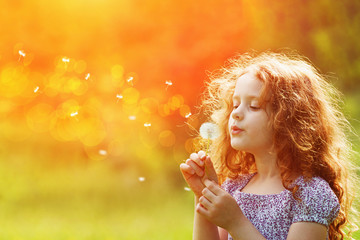 Beautiful child enjoy blowing dandelion in spring park.