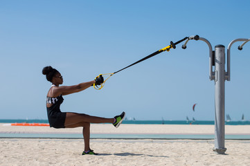 Young woman of african ethnicity balancing using special ropes for suspension training. Outdoor sport activity concept - obrazy, fototapety, plakaty