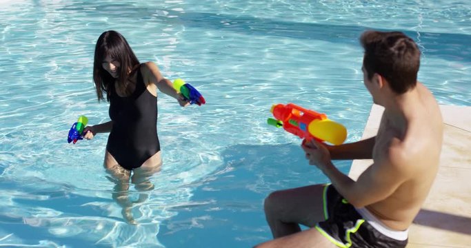Young adults shooting shooting plastic water guns at each other in swimming pool outdoors