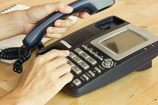 Female Hand Holding Phone Receiver And Dialing Number In Workplace